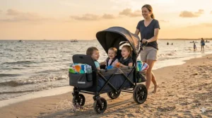 Two toddlers sitting in an all-terrain double stroller wagon with rugged wheels on a sandy beach.