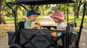 A candid, high-detail photograph looking closely inside the fabric cabin of the dark grey Jeep wagon stroller, showing the older boy with his teddy bear and the older girl face-to-face, laughing and sharing snacks in the warm natural sunlight of a park.