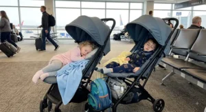 Two toddlers napping comfortably in fully reclined seats of a lightweight double stroller during a flight layover.