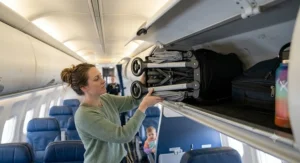 Passenger stowing a compact double stroller into an airplane overhead storage compartment.
