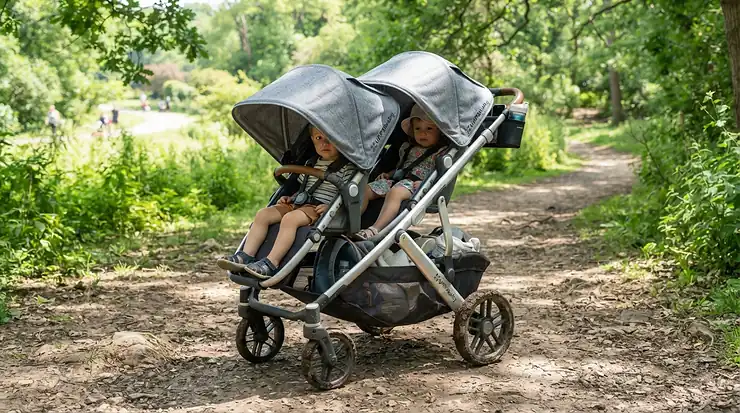 An all-terrain twin jogging stroller for trail runs with extended sun canopies lowered on a bright afternoon.