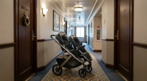 A compact twin stroller for cruise vacations fitting easily down a narrow cruise ship corridor outside a cabin door.