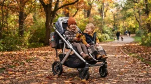 Children enjoying the ride in a single-to-double stroller for close-in-age siblings surrounded by fallen autumn leaves.
