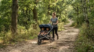 A father navigating a gravel nature trail with a twin jogging stroller for infant twins.